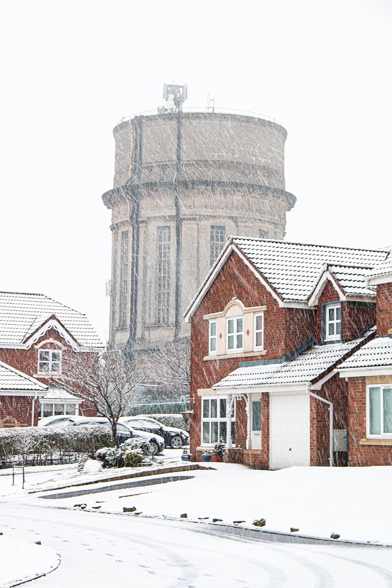 Residential street with snow falling and water tower in background